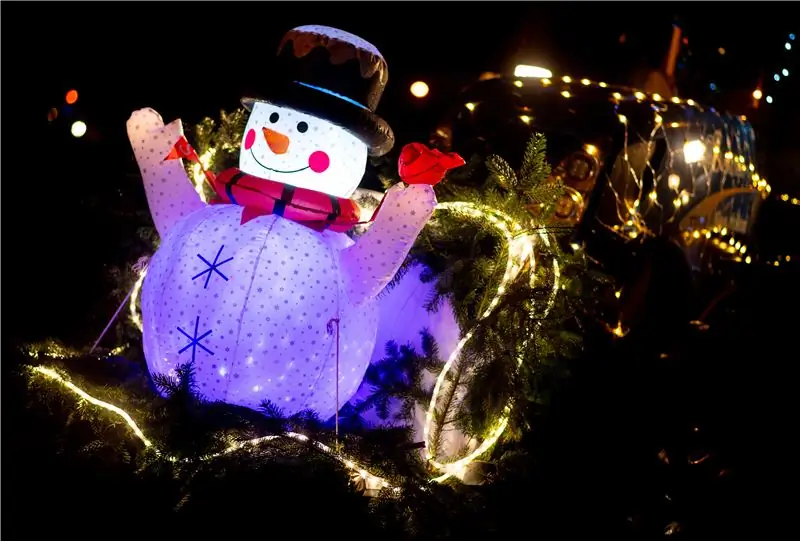 Светящийся снеговик стоит на тракторе, украшенном к Рождеству