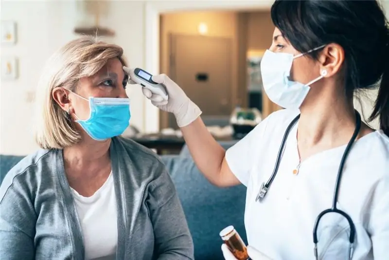 пожилая женщина измеряет температуру медсестре covid