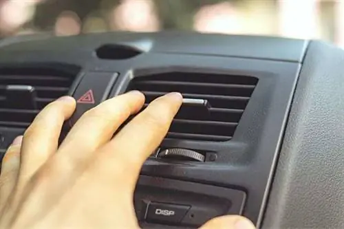Человек, касающийся вентиляционного отверстия кондиционера в своей машине