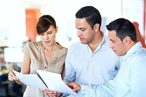 Трое человек смотрят на два листа, которые держат в руках.