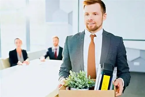 Мужчина в костюме держит коробку с вещами, а за ним другие люди