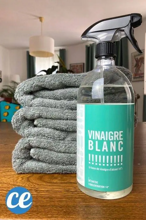 Бутылка белого уксуса перед кучей чистых пушистых махровых полотенец.