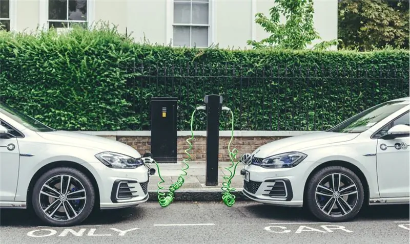 Два белых автомобиля Volkswagen Golf GTE заряжаются на зарядной станции на одной из улиц Лондона.