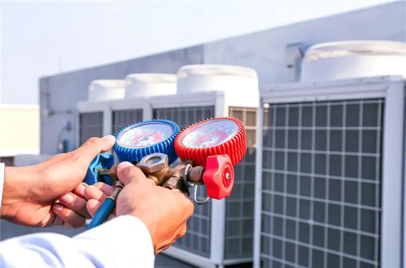 Техническое обслуживание и обслуживание кондиционера, крупный план ручного механика с помощью измерительного манометра для заполнения промышленных заводских кондиционеров, очистки и проверки ремонта компрессора наружного воздуха.