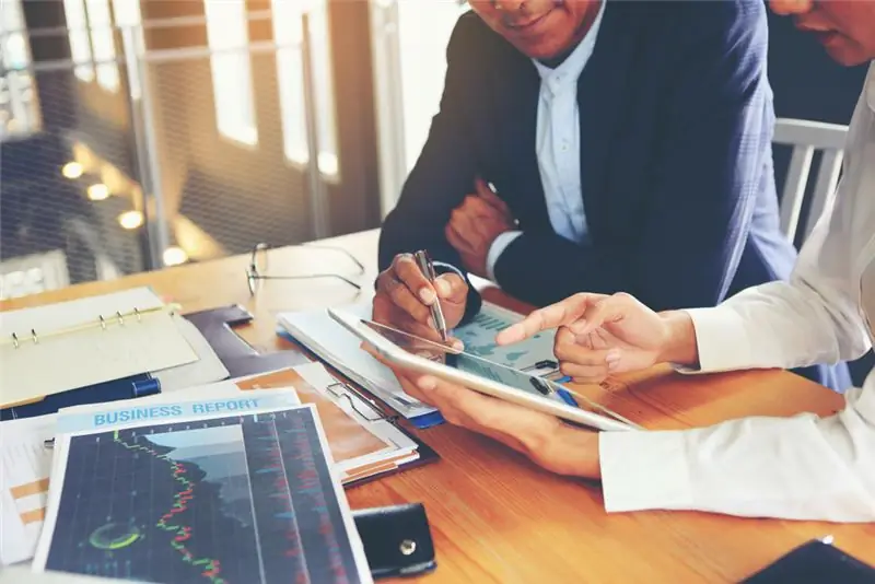 Люди сидят за столом и смотрят на планшет во время встречи.