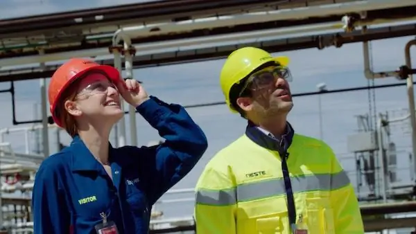 Женщина и мужчина в строительном снаряжении смотрят вверх и улыбаются.