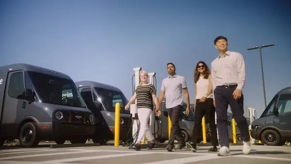 Четыре человека идут по парковке, заполненной фургонами доставки.