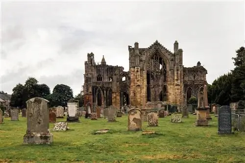 Аббатство Мелроуз стоит крепко в пасмурный день, окруженное могилами, датированными на всем протяжении