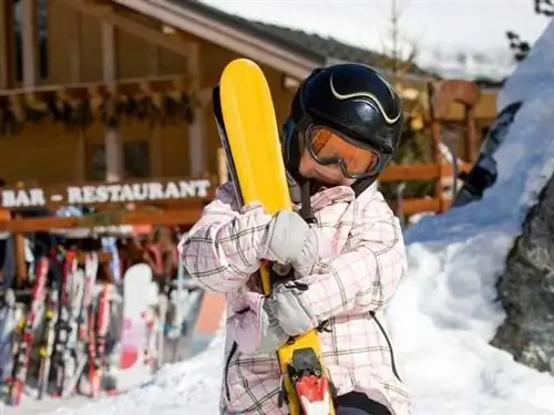 Ребенок держит пару лыж возле шале.